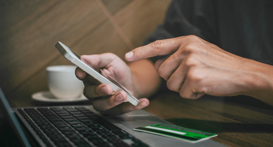 Close-up of hands using a smartphone and laptop with a credit card nearby, representing buying Canadian weed online with Supreme Dispensary