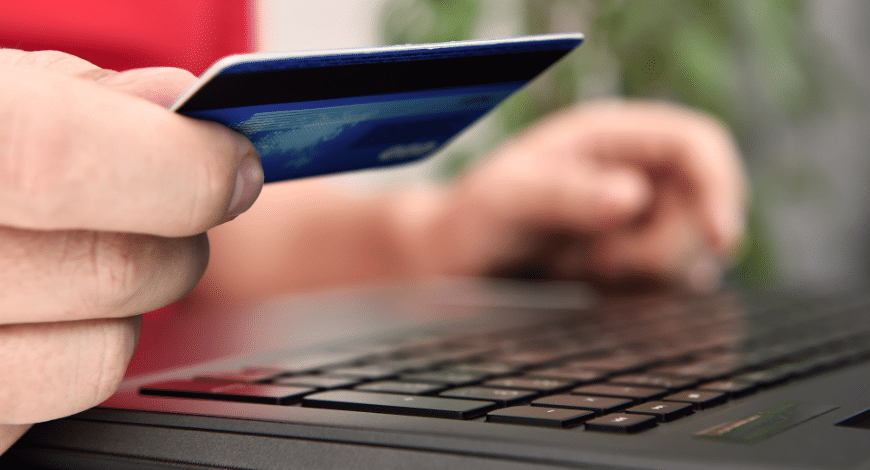 A person holding a credit card while using a laptop, representing shopping online for the Mimosa cannabis strain today