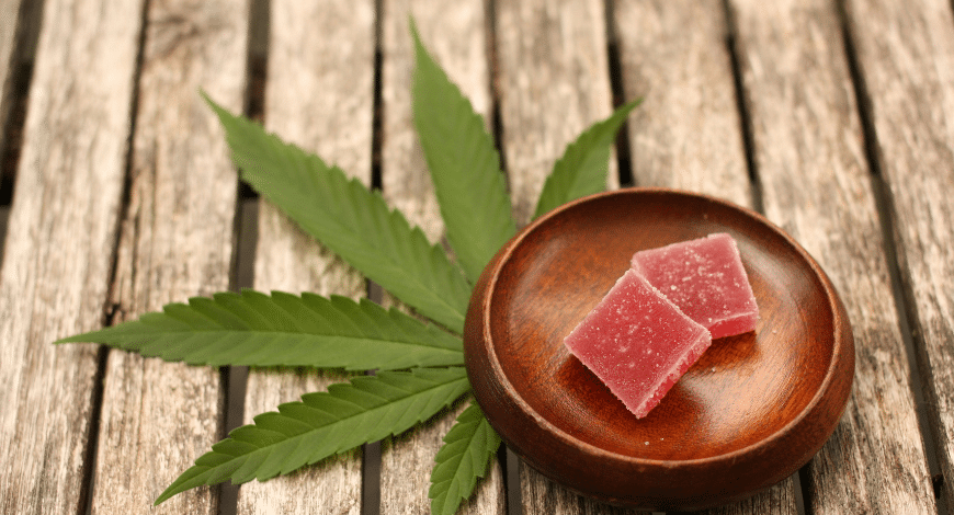 Two red cannabis gummies in a wooden bowl placed on a cannabis leaf, illustrating what to expect from strong edibles in Canada