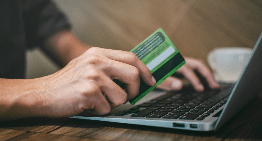 Close-up of hands using a laptop and holding a green credit card, representing where to buy Gas Mask weed online in Canada