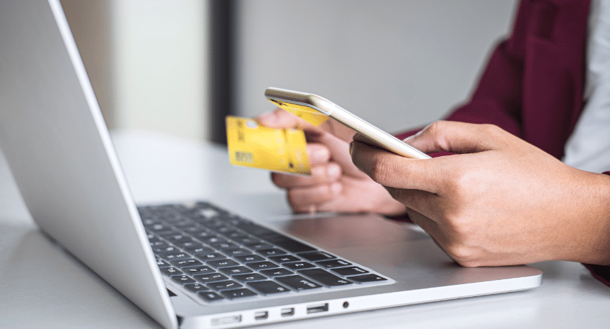 Person holding a credit card and smartphone while shopping on a laptop, representing where to buy weed online